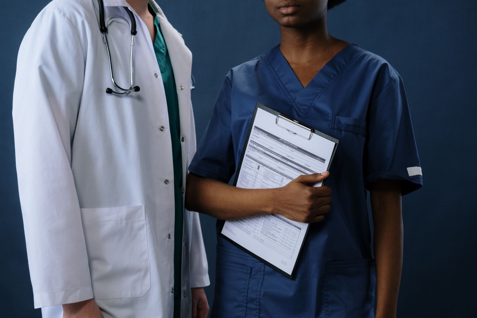 Krankenhaus – zwei Mitarbeitende in blauer Dienstkleidung mit Klemmbrett